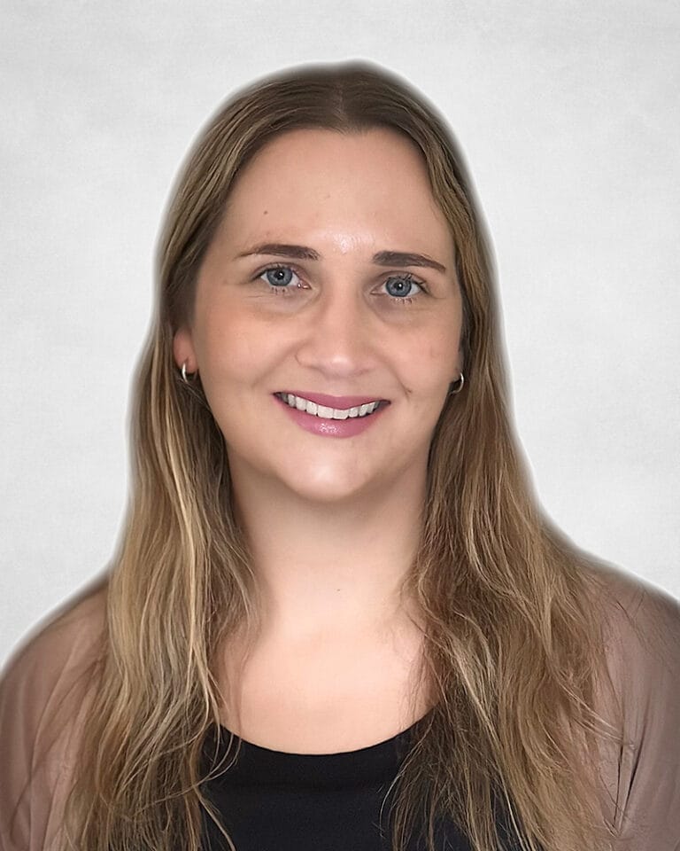 Alana Bancsecue is a woman with long, light brown hair and blue eyes. She is wearing a black top and a brown sheer cardigan.