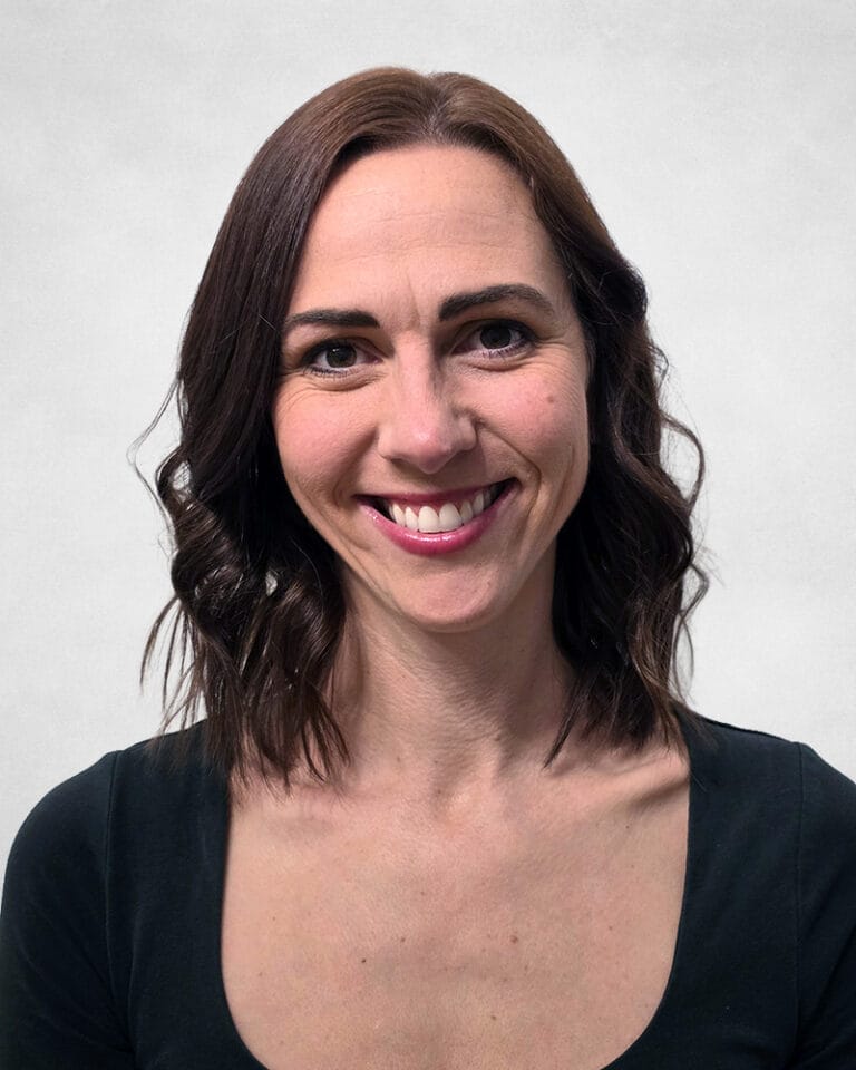Ashley Nickel is a woman with shoulder-length brown wavy hair. She is wearing a dark top with a round neckline.