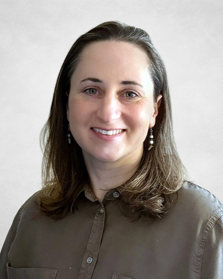 Esther Rottenstreich has straight, shoulder-length brown hair. They are wearing a brown button-up shirt and dangling earrings.