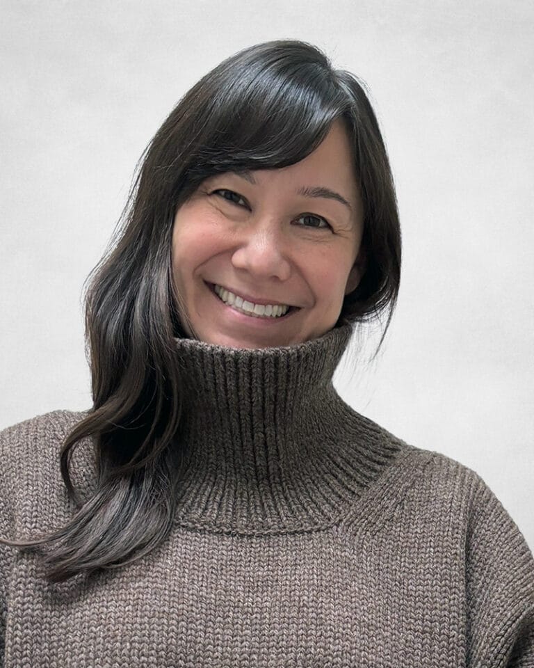 Jennifer Sawrenko is a woman with long black hair and a warm smile. She is wearing a grey and textured turtleneck sweater.