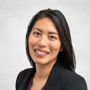 Jessica Lee is a woman with long black hair. She is wearing a black blazer and burgundy top.