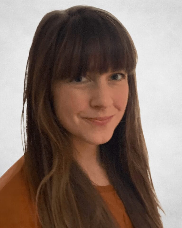 Kendall Miller is a woman with long brown hair and a fringe, wearing an orange top.