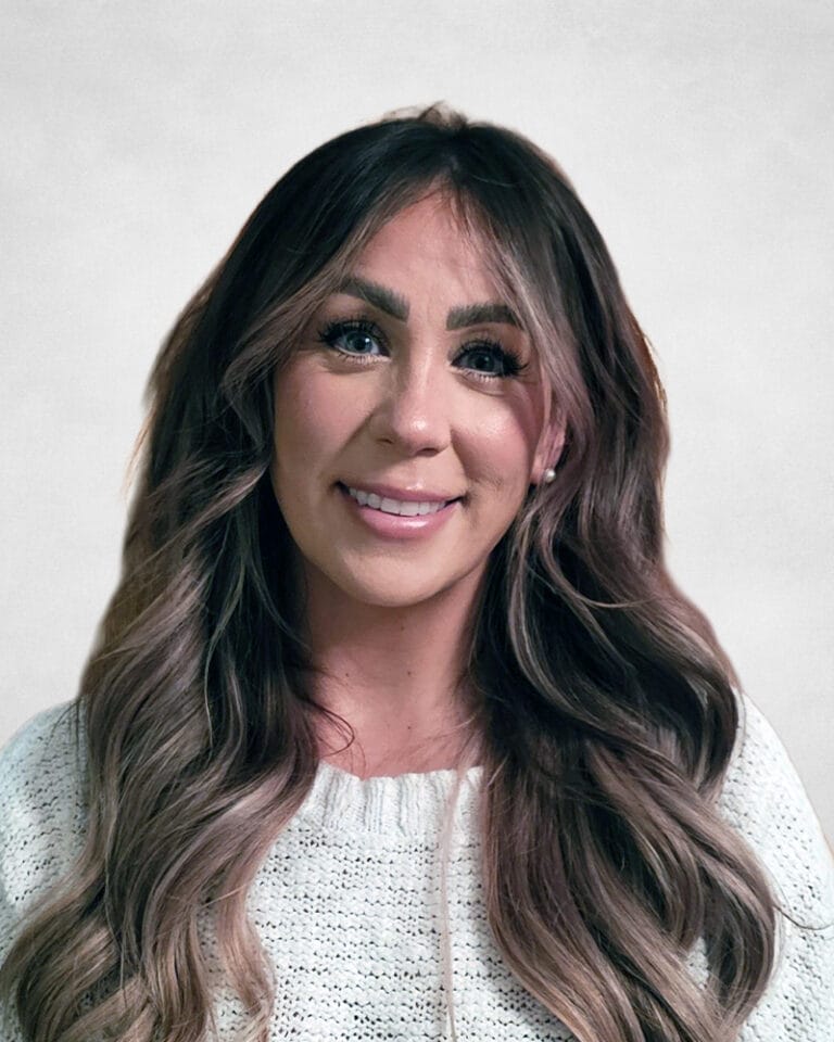 Lauren Saunders is a woman with long, wavy brown hair and is wearing a white knitted sweater.