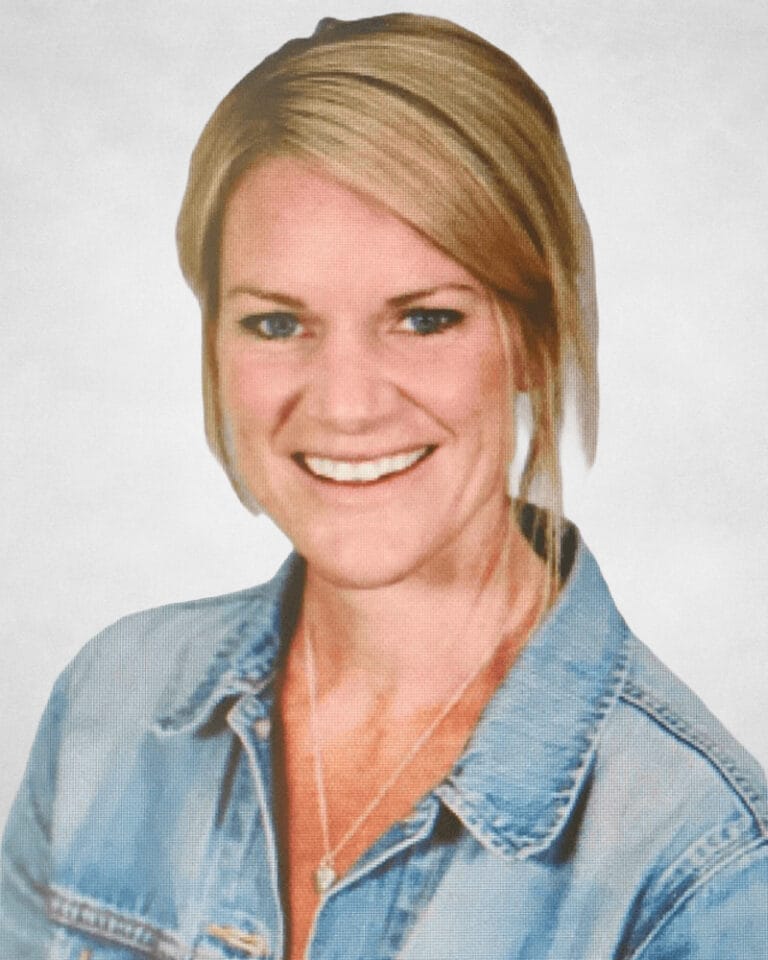 Mikki Zuiches is a woman with blonde hair, styled to the side. She is wearing a light blue denim jacket over a white top and a silver necklace.