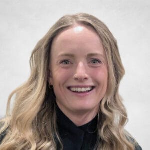 Montana Bahen is a smiling woman with long, wavy blonde hair. She is wearing a black top.