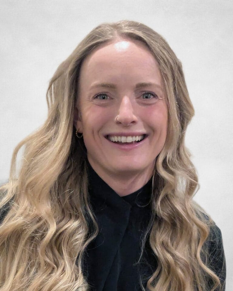Montana Bahen is a smiling woman with long, wavy blonde hair. She is wearing a black top.