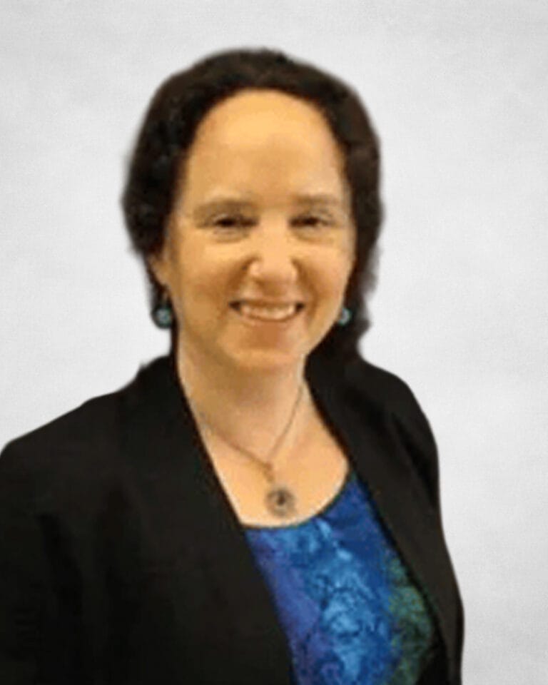 Sandra Lamb is a woman with short, curly dark hair. She is wearing a black blazer over a blue patterned top, with turquoise earrings and a pendant necklace.