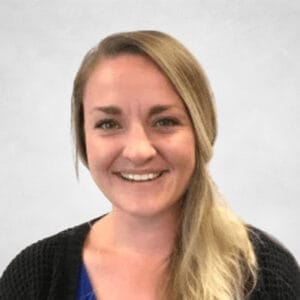 Taylor Schmidt is a woman with long blonde hair. She is wearing a blue top and a black cardigan.