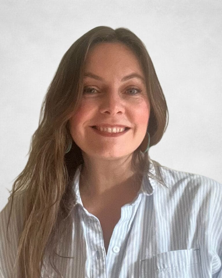 Thea Borserio is a woman with long brown hair. She is wearing a light blue and white striped button-up shirt.